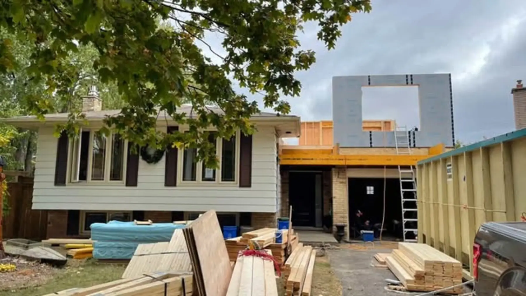Second-storey framing going up over the Burlington bungalow, with lumber staged in the driveway
