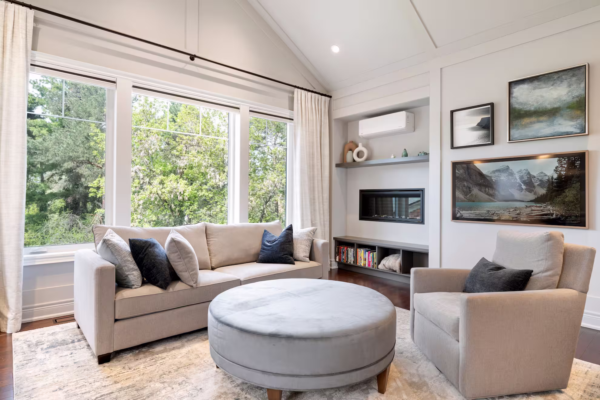 Living room with a bay window, sectional seating and a round upholstered ottoman
