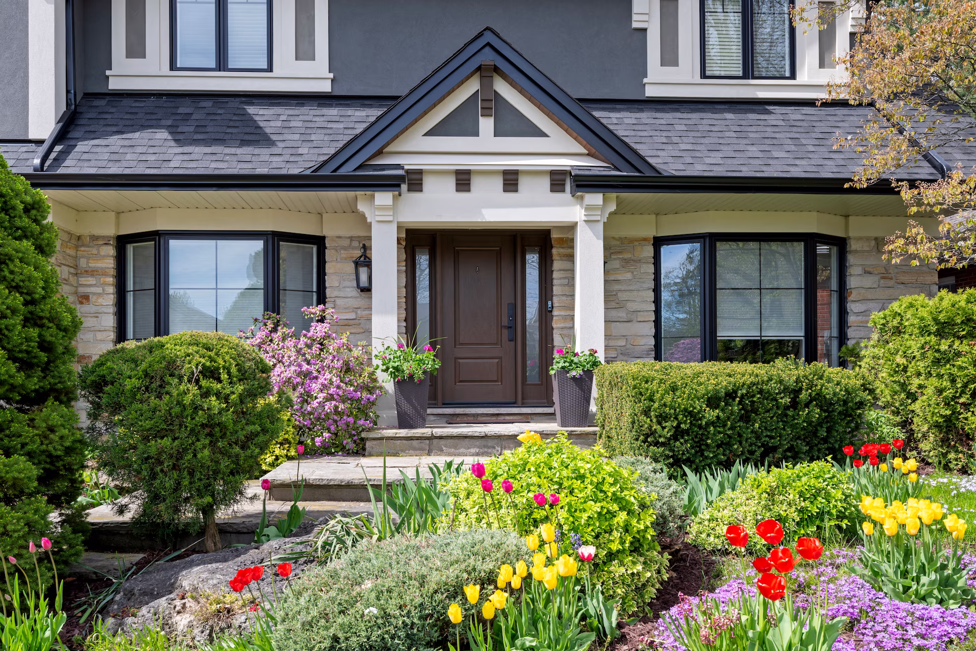 Covered front entry with dark wood door and spring garden beds, Waterdown second-storey addition