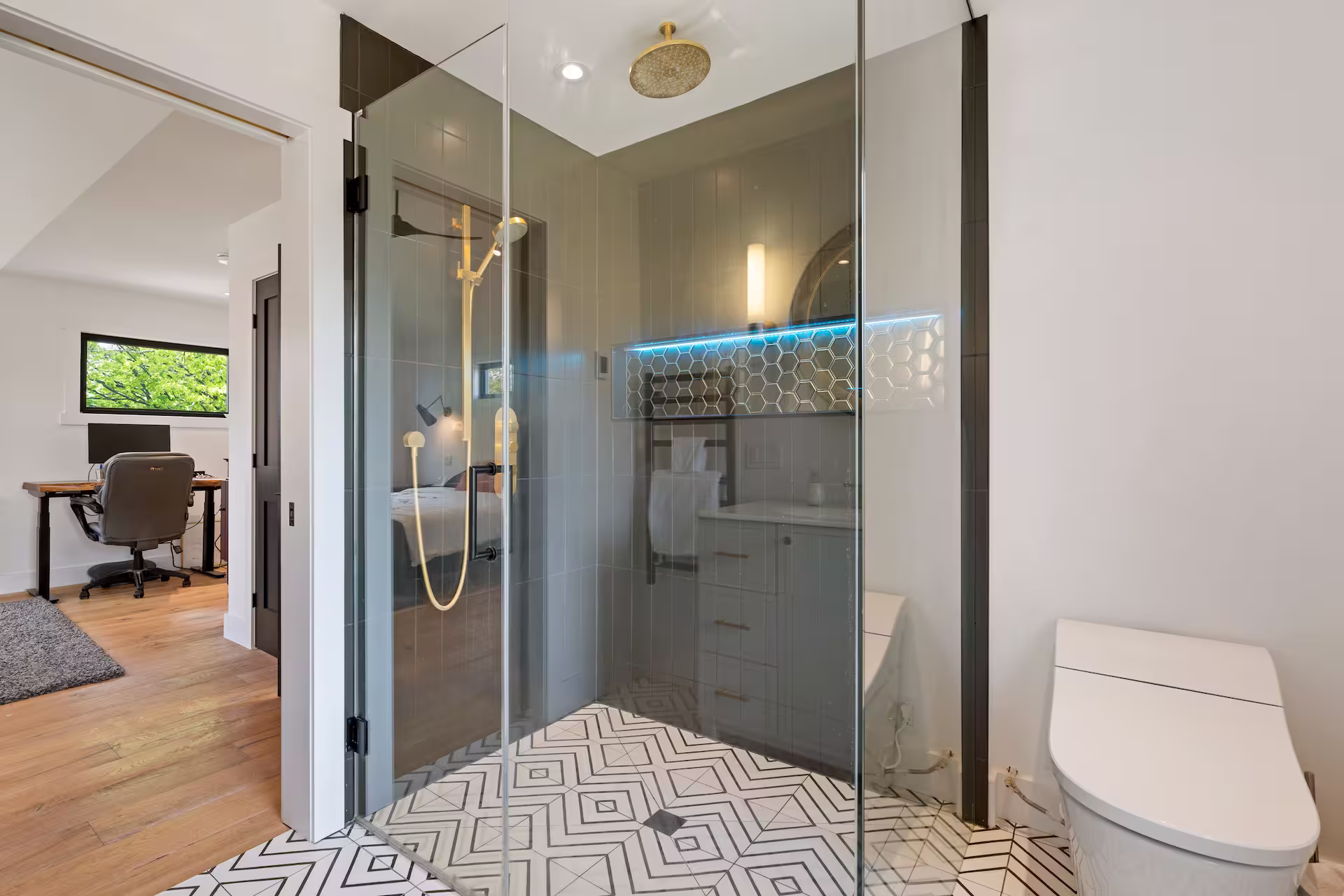 Walk-in glass shower with dark tile surround, viewed from the hallway of a renovated bathroom