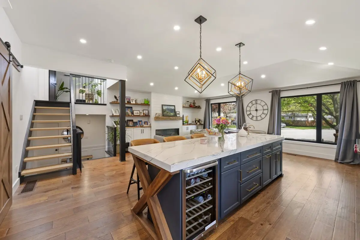 Open main floor with a dark kitchen island, open-riser staircase and hardwood flooring