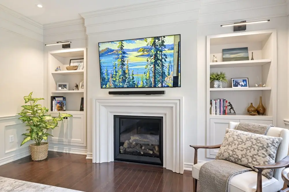 Living room fireplace flanked by white built-in shelving with a television mounted above