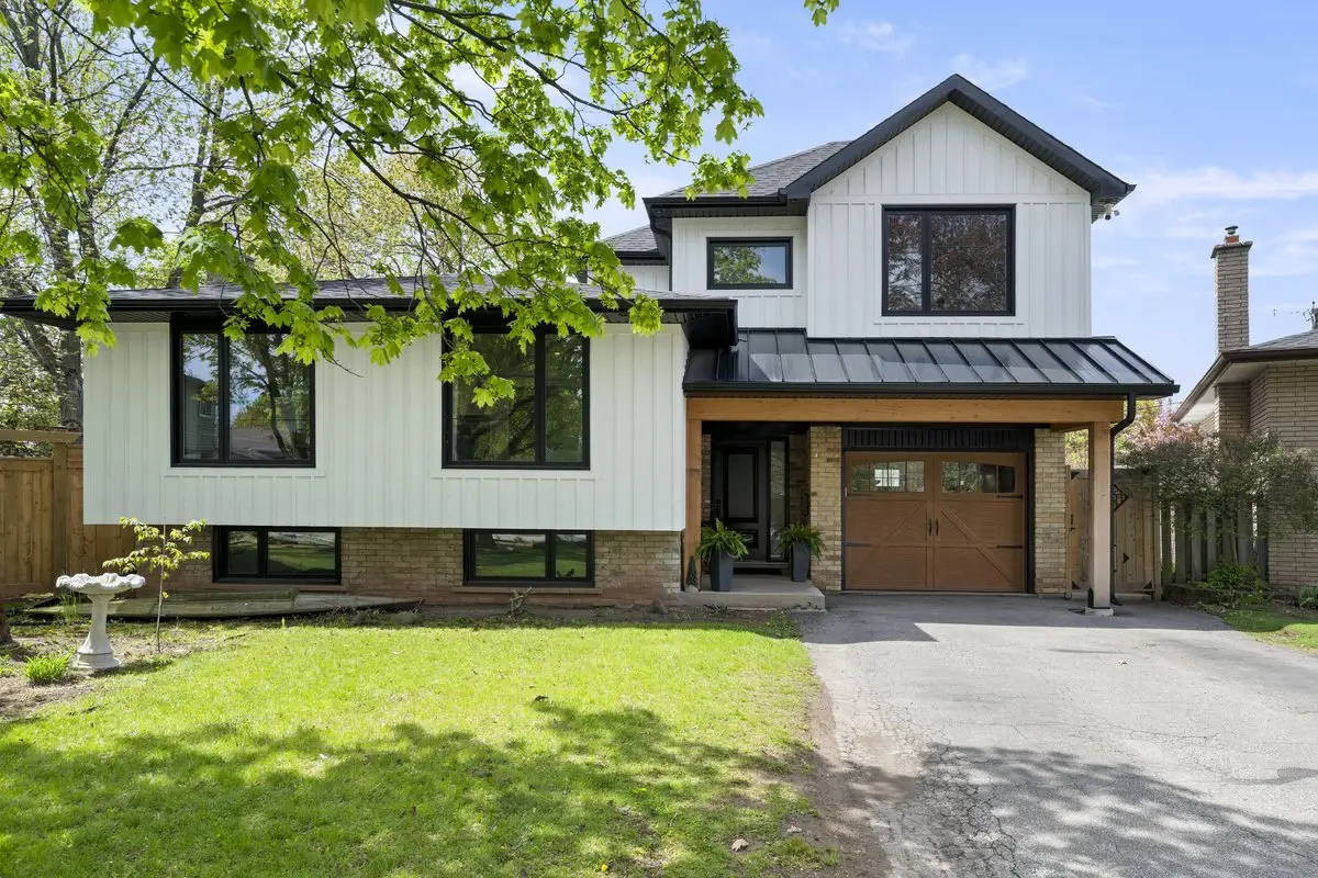 Renovated split-level home with white board-and-batten siding, black windows, a standing-seam metal roof over the entry and a wood garage door