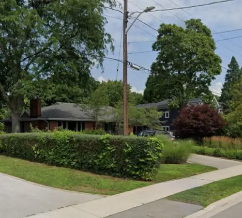 Street view of a single-storey home behind a mature hedge