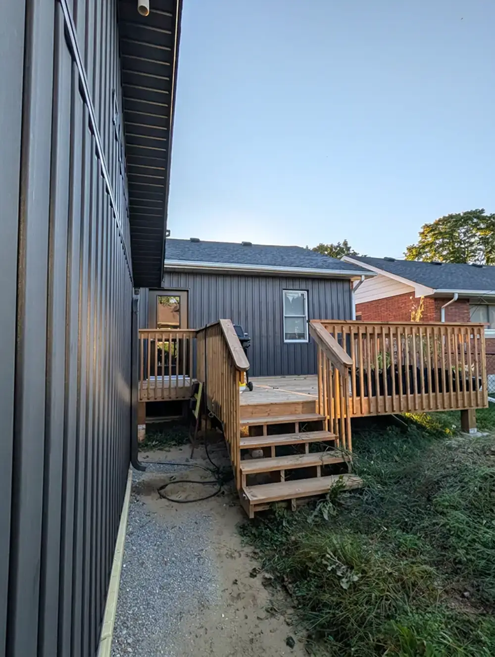 Pressure-treated wood deck and stairs beside a new accessory dwelling unit with dark board-and-batten siding