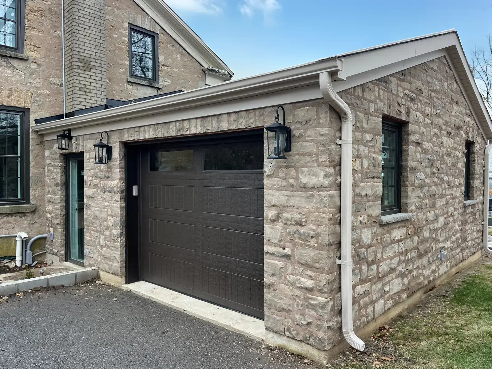 Attached single-car garage clad in stone to match the house, with a black overhead door and carriage lights