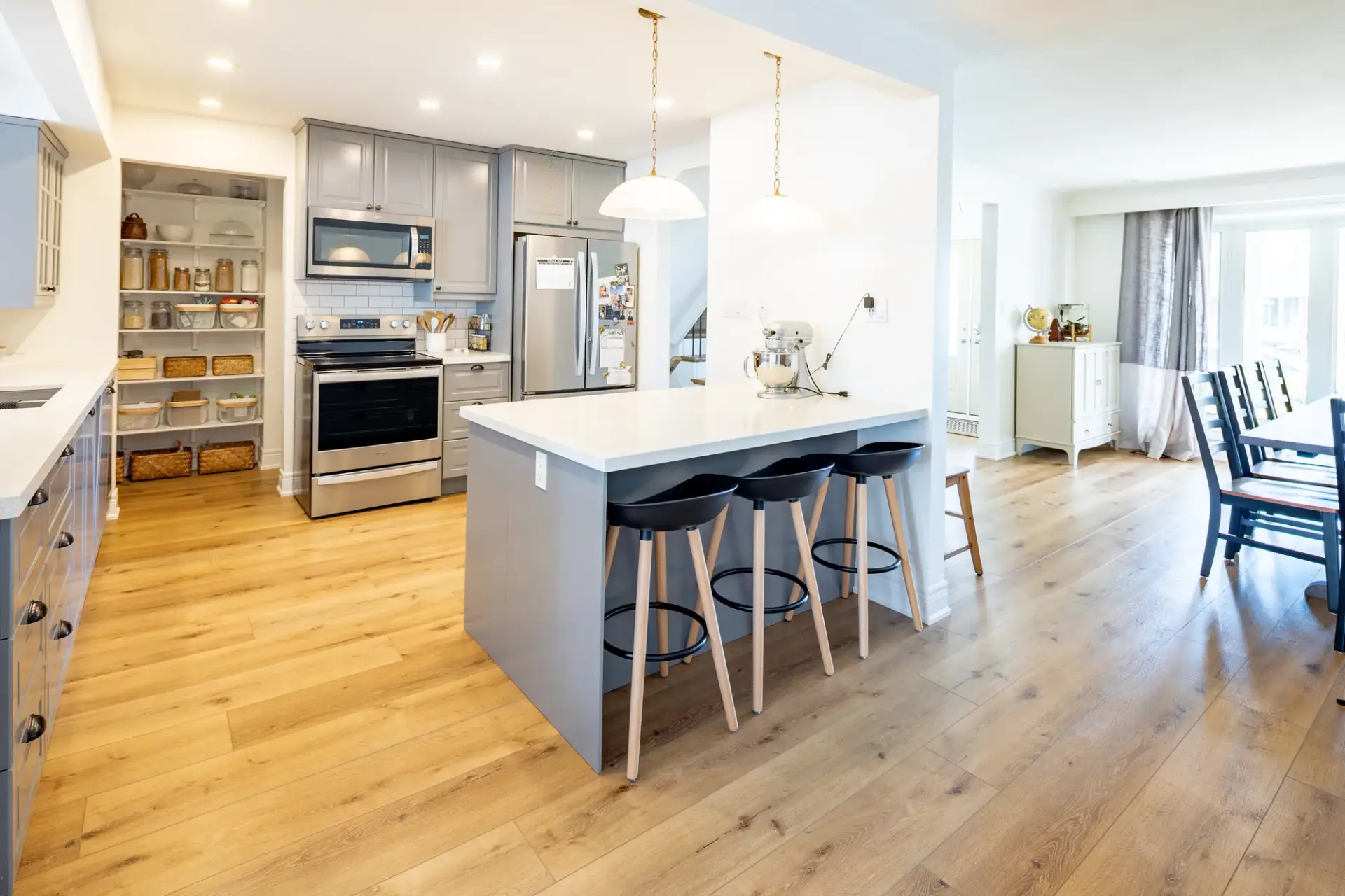 Kitchen with a dark island, counter stools, stainless appliances and light wood flooring
