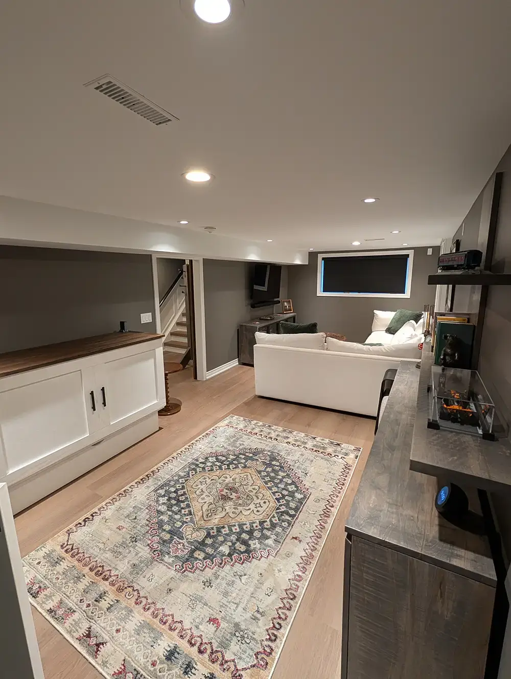 Finished basement lounge with white built-in cabinets, a patterned area rug, sectional sofa and wall-mounted TV