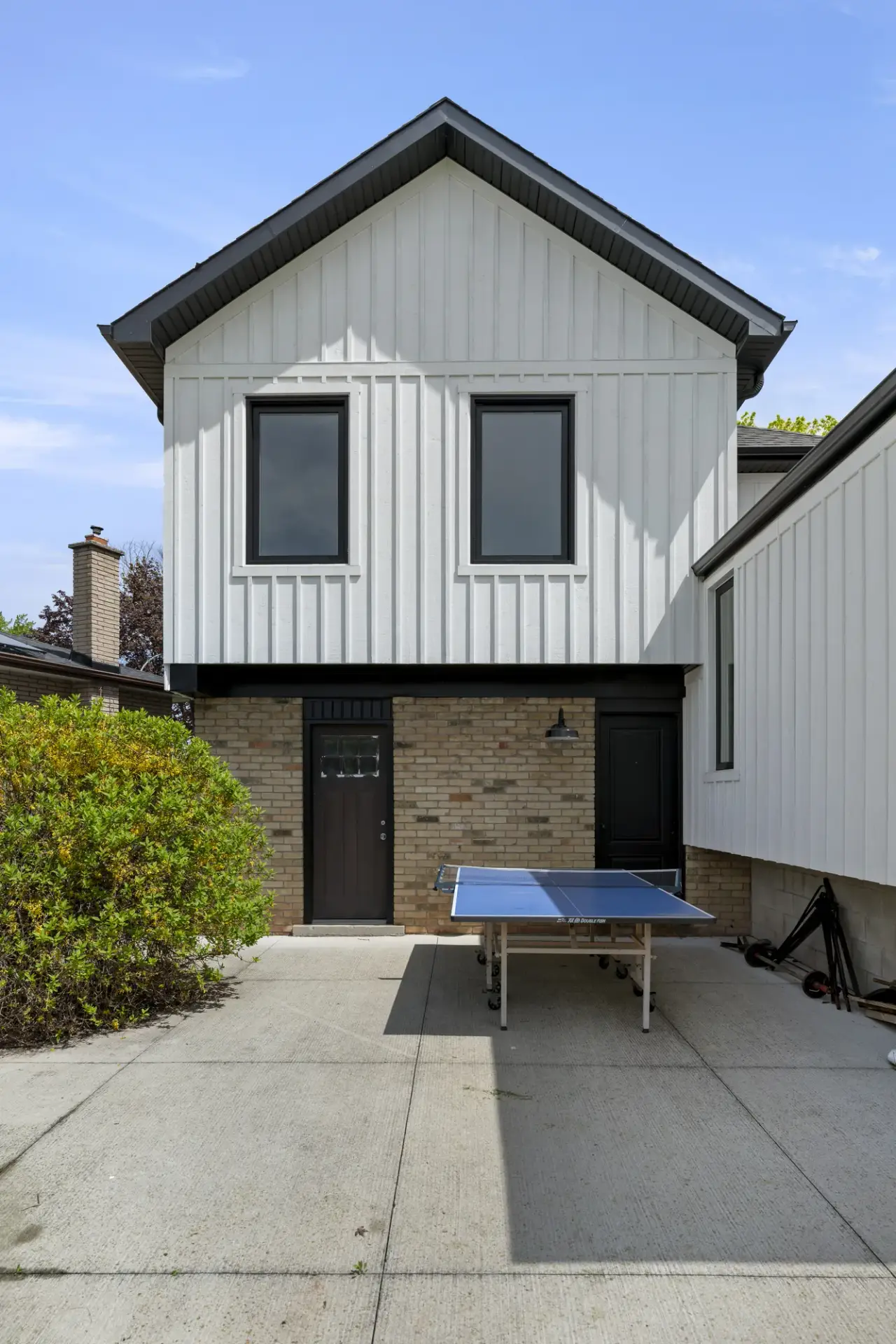 Exterior detail where new board-and-batten siding meets the original brick beside a dark door
