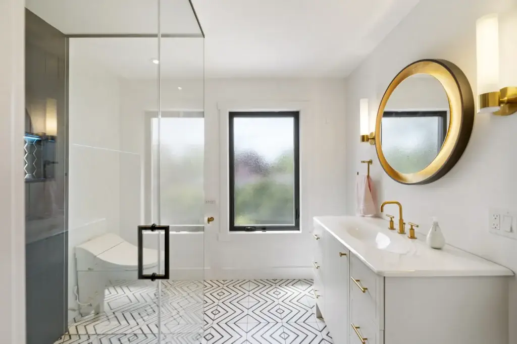 Ensuite with a round gold-framed mirror, glass shower and windows above a soaker tub