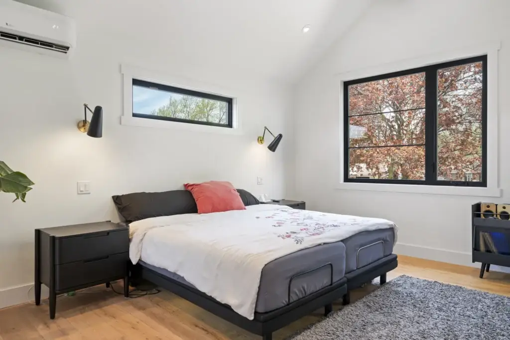 Bedroom with a black-framed picture window, wall sconces and a dark upholstered bed