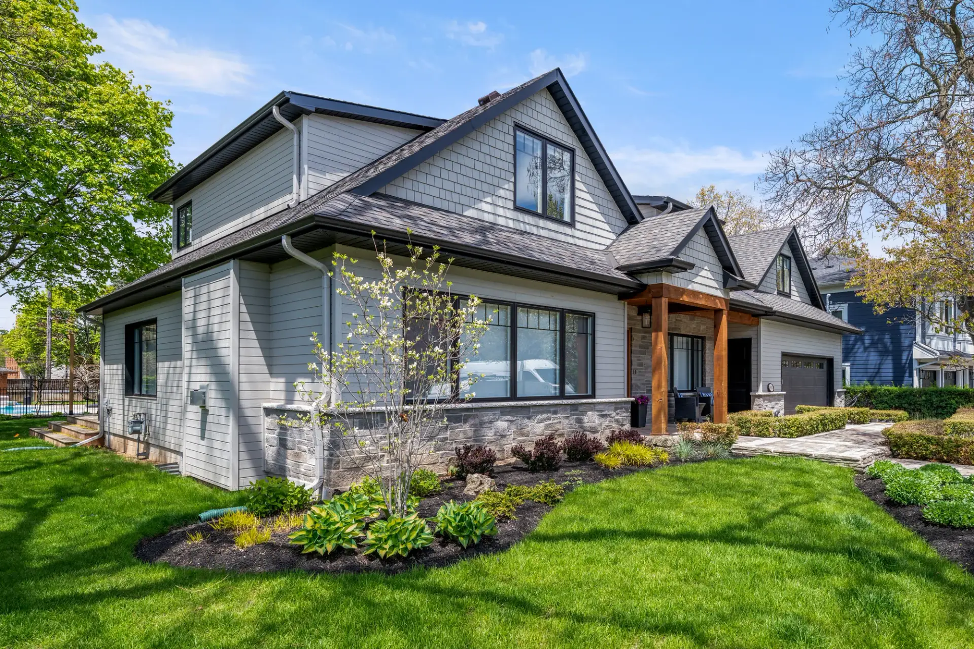 Two-storey home exterior with grey shingle siding, stone accents and landscaped garden beds