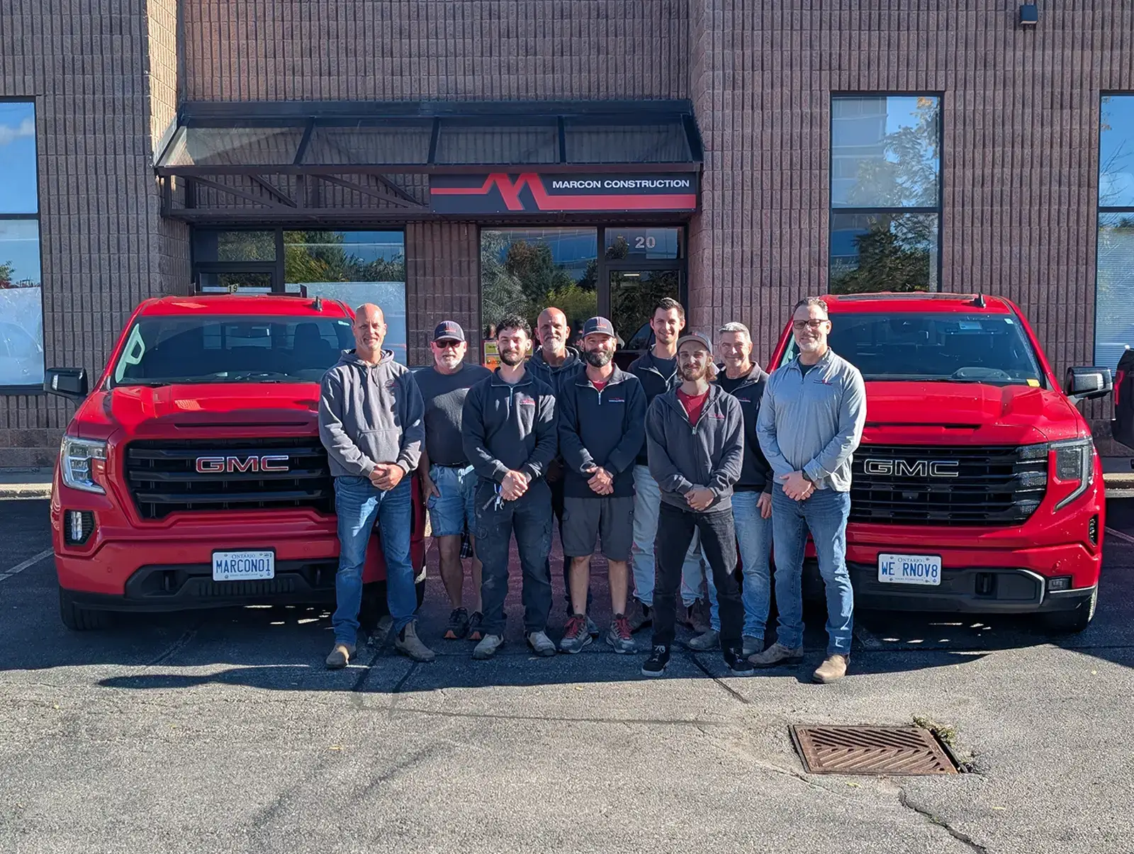 The Marcon Construction team standing outside the office with their red company trucks parked behind them